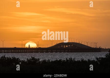 The Port Isabel Lighthouse in front of the setting sun with the Queen Isabella Memorial Bridge to the right.  Texas.  Viewed across the Laguna Madre f Stock Photo