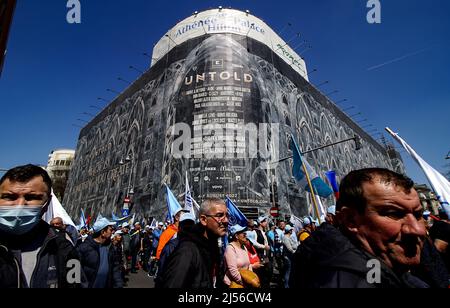 Bucharest, Romania - April 06, 2022: Protesters at a union rally pass by an advertisement for Untold Festival on a very large banner on Athenee Palace Stock Photo