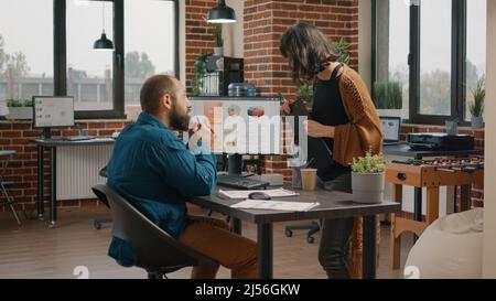 Business man asking for help from woman to design rate charts on computer monitor. Entrepreneur and colleagues doing teamwork to plan data analysis on display for startup presentation. Stock Photo