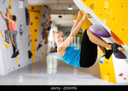 Woman climbing tall, indoor, man-made rock climbing wall Stock Photo