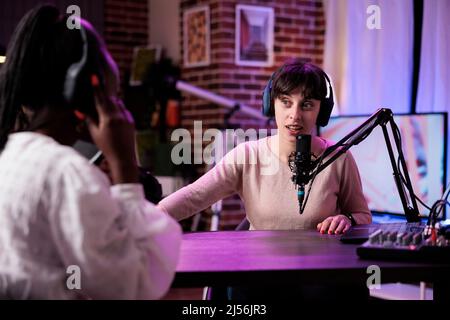 Content creator having conversation with female guest, recording podcast with sound equipment. Influencer talking to cheerful woman to broadcast live discussion to record in studio. Stock Photo