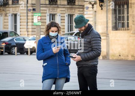 Picture of a white caucasian couple, male and female in Bordeaux, France checking her smartphone in the streets of Bordeaux, while wearing a respirato Stock Photo