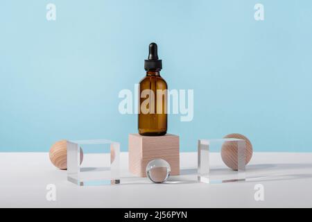 Oil cosmetics amber product packaging with stylish props. Serum cosmetic bottle with peptides and retinol on acrylic and wooden blocks on blue Stock Photo