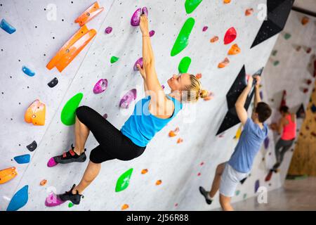 Woman climbing tall, indoor, man-made rock climbing wall Stock Photo