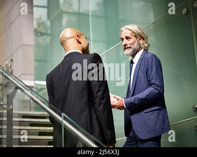 caucasian and latino corporate business men talking chatting having a conversation while walking on stairs in modern office building Stock Photo