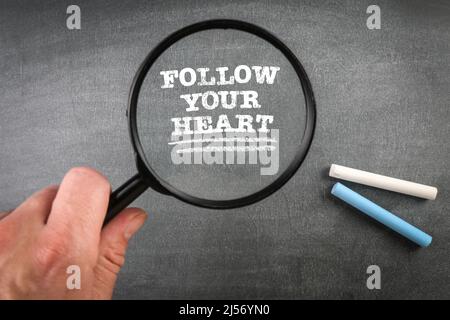 Follow Your Heart. Magnifying glass and pieces of chalk on a dark board. Stock Photo