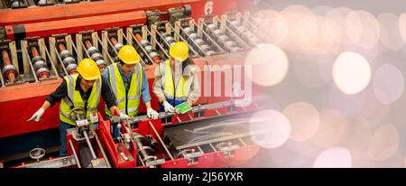 Engineer and operator wearing a safety suit maintaining machine in industrial metal sheet factory, team worker walk teaching help friend operate contr Stock Photo