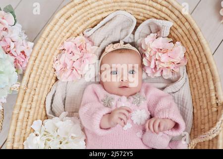 Cute baby girl in knitted clothes and wreath with teddy bear toy. Spring background with flowers. Children Protection Day. Mother's day greeting card. Stock Photo