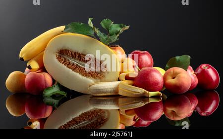 Fresh fruits on a black reflective background. Apples, bananas, melon, pears, and peaches are presented. Stock Photo