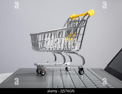Supermarket trolley at laptop. Online shopping concept. Buying goods using Internet. Electronic trade and transactions. Purchases in web stores. High quality photo Stock Photo