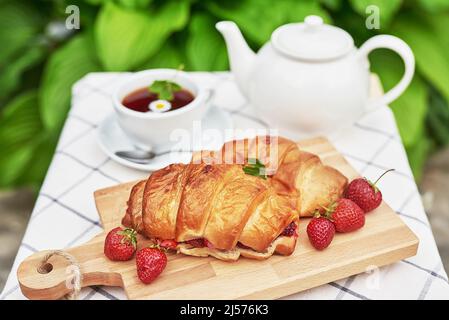 Breakfast outside. Cup of tea, strawberries, cherries, croissants on table. Summer picnic. Good morning concept Stock Photo