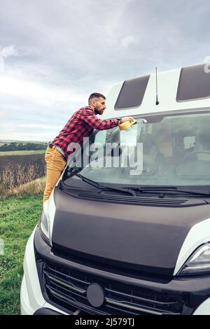 Man cleaning camper van windshield outdoor Stock Photo