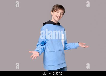 Positive studio portrait cute toothy smiling young caucasian guy isolated on gray copy space. Happy teenager wearing a blue sweatshirt looking at the camera. Cheerful guy gesturing cheerfully Stock Photo