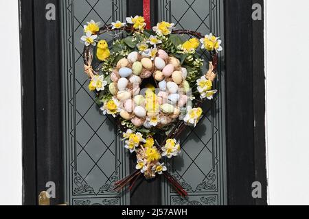 An Easter wreath in the shape of a heart made of hazel wood branches, yellow baby chicks, daffodils and painted eggs, Easter celebration Stock Photo