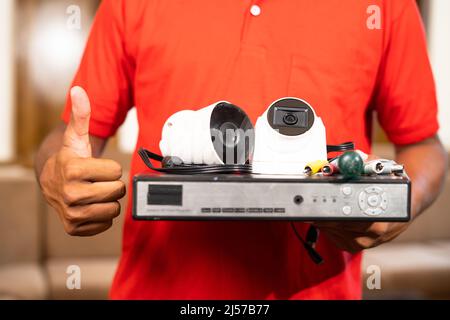 close up shot of technician showing thumbs up gesture by holding cctv camera equipments in hand - cocnept of recommendation, approval and professional Stock Photo