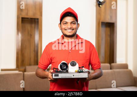 Smiling electrician with cctv camera and equipments in hands by looking camera at home - concept of professional occupation, saftey and recommendation Stock Photo