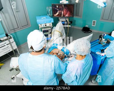 Doctors look at the monitor and operate on the patient. Top view of a team of surgeons performing laparoscopic surgery. Stock Photo
