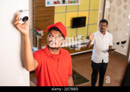 Technician fixing angle or view of cctv camera by while customer checking in digital tablet at home - concept of professional occupation, employment Stock Photo