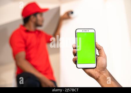 Close up shot of hands showing green screen mobile phone while while electrician fixing cctv camera at home - concept of online booking, advertisement Stock Photo