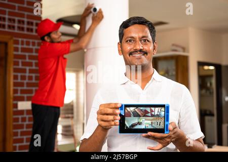 House owner showing cctv camera footage on tablet in front of technician fixing camera at home - concept of surveillance, safety secure and technology Stock Photo