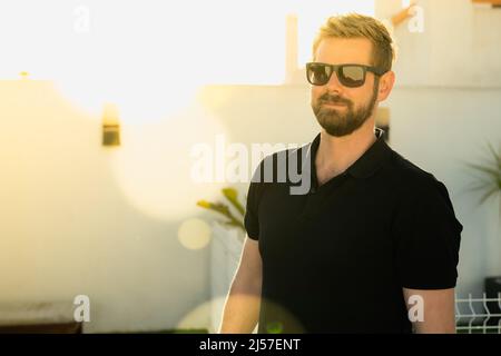 Hipster handsome male model with beard wearing black polo shirt with space for your logo or design in casual urban style Stock Photo