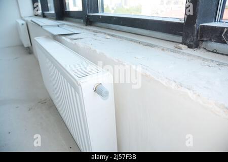 Installing radiator heating with thermostat in the unfinished empty room. Stock Photo