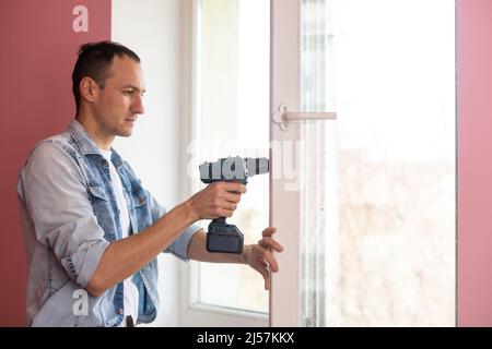 Handyman using a cordless screwdriver to install a window handle. Qualified worker services, home repair and renovation. Stock Photo