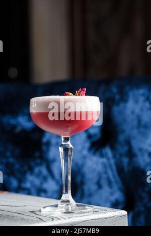 Pink Clover Club Cocktail in Coupe Glass with Layer of Foam and flower Garnish isolated on dark Background. Stock Photo