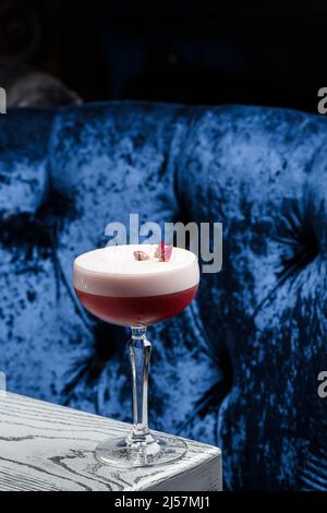 Pink Clover Club Cocktail in Coupe Glass with Layer of Foam and flower Garnish isolated on dark Background. Stock Photo