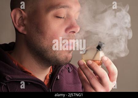 Smoking medicinal marijuana. Young man smoking CBD cannabis with a bong. Weed smoker's close-up portrait with a lot of fume. Marihuana effect for medi Stock Photo