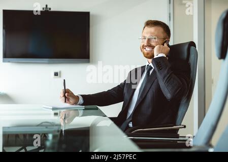 Businessman and head of the company are sitting at the table alone in the office meeting room and talking on the phone Stock Photo