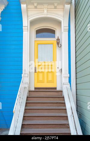Entrance of a house with ornate columns and wooden doorsteps at San Francisco, California. Porch of a house with yellow front door and transom window Stock Photo