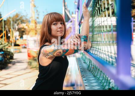 Portrait of a tanned young woman with tattoo sleeve posing near a fence. The concept of freedom and psychology. Stock Photo