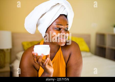 hispanic woman with towel on head applying cream on face at home skin positivity Stock Photo