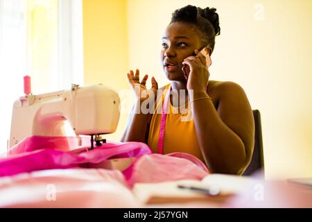 african american woman tailor creates a collection of outfits talking with client by phone Stock Photo