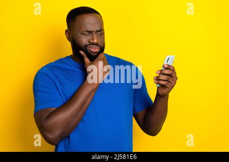 Portrait of attractive minded supicious guy using device deciding post smm follow isolated over shine yellow color background Stock Photo