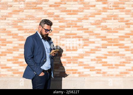 Adult man using phone against brick wall Stock Photo