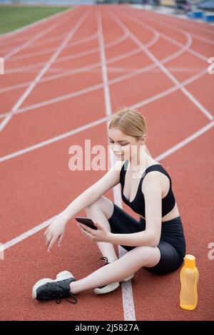 young sportive woman sitting with crossed legs and using cellphone Stock Photo