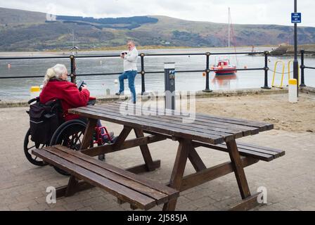 A wheelchair user on mobile phone at Barmouth harbour in North Wales Stock Photo