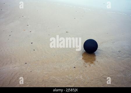 A black football on the sandy seashore at Barnouth, North Wales Stock Photo