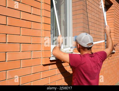 Mosquito wire screen installation. Contractor installing mosquito wire screen on house window to protect from insects. Stock Photo