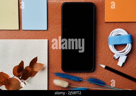 knolling composition of smartphone, wrapped charging cord, dry twigs and adhesive notes on leather surface Stock Photo