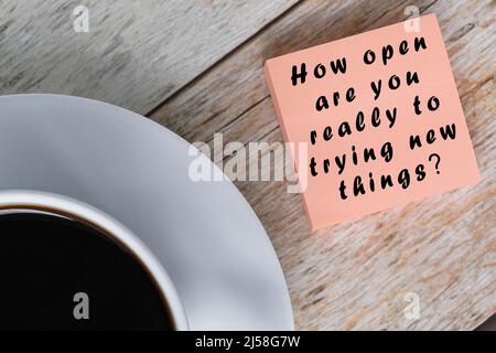 Motivational quote on notepad with white coffee cup on wooden desk - How open are you really to trying new things. Questions. Stock Photo