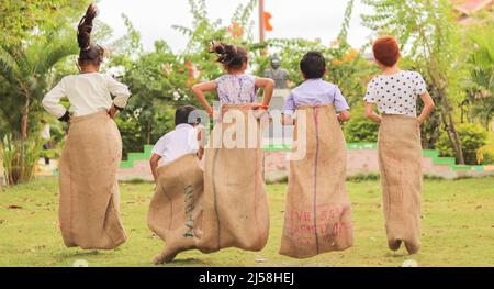 back view shot of Group of Childrens playing potato sack jumping race game at park during summer camp - concept of childhood physical activities and Stock Photo