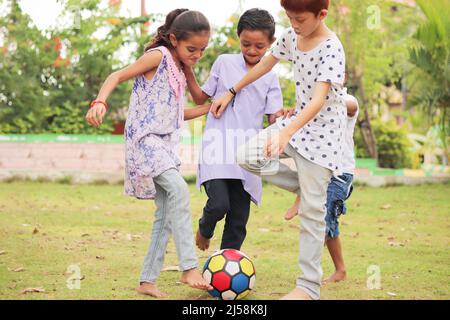 group of multiethnic diverse kids playing football at park - concept of summer vacation, holidays, active childhood lifestyle Stock Photo