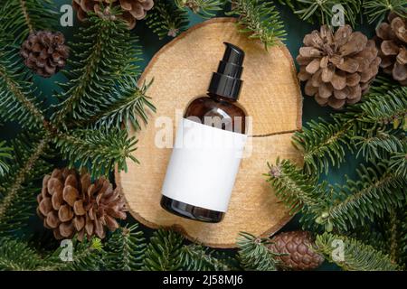 Brown glass bottle between fir branches and pine cones on wooden piece top view. Brand packaging mockup. One pump dispenser for skincare product, crea Stock Photo
