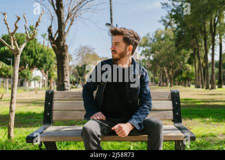 Young man looking thoughtfully ahead, the man waiting for his friend while sitting is wondering what is going on ahead, thoughtful anticipation Stock Photo