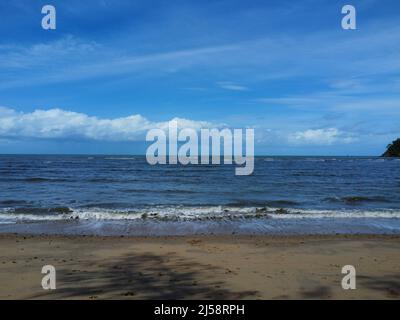 View of waves crashing onto beach with blue sky Stock Photo