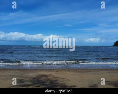 View of waves crashing onto beach with blue sky Stock Photo