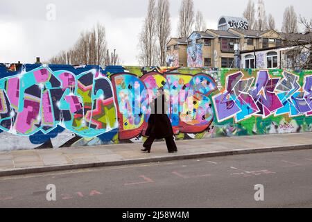 People person walking by colourful graffiti painting on hoardings in Brick Lane Shoreditch spring April 2022 London England UK  KATHY DEWITT Stock Photo